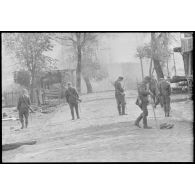 Dans la rue d'un village désert, des fantassins sont à la recherche de mines.