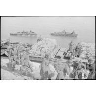 Après la traversée d'une rivière sur un ponton (Brückengerät), le personnel gagne la berge, tandis que des sacs postaux vont être déchargés.