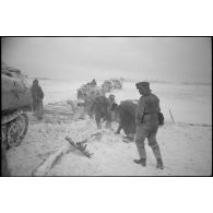 Un semi-chenillé a versé d'un pont de bois, des fantassins tentent de consolider le pont pour le passage d'autres véhicules.