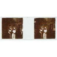 [Deux infirmières cueillent des fleurs devant un bâtiment].<br>