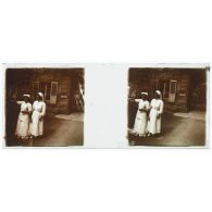 [Deux infirmières cueillent des fleurs devant un bâtiment].<br>