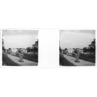 [Soldat, jumelles sur la poitrine, posant sur un chemin ; ruines à l'arrière-plan].