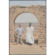 Un officier du DMAT d'Atar pose en compagnie d'un guide maure sous l'arche des ruines du décor de cinéma réalisé pour le film "Fort Saganne". [légende d'origine]<br>