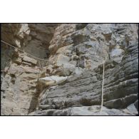Formation des aides moniteurs commando et des élèves officiers de l'école militaire interarmes d'Atar à l'escalade et au rappel, aux techniques de cordes et d'assurance, au franchissement de fortune, au brancardage dans les falaises de l'Oued Illïj, région d'Atar et d'Azougui. Température d'exercice avoisisant les 40° en raison du rayonnement sur les parois rocheuses, 300 élèves et 10 aides moniteurs ont été formés pendant cette période. [légende d'origine] <br>