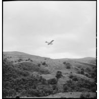 Un avion d'observation Piper Cub survolle la zone kabyle où se déroule une opération.