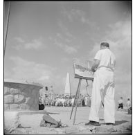 Plan en contre-plongée en pied d'un peintre qui reproduit une scène de la commémoration célébrant le centenaire des combats de Sidi-Brahim.