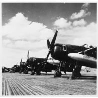 Des avions de chasse Bearcat du GC 1/8 Saintonge chargés de bombes au napalm alignés sur le sol d'une base aérienne.