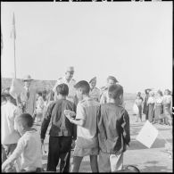 Le général de Linarès et une assistante sociale parcourent le village Muong de Kobe au milieu des enfants occupés à jouer avec les cadeaux qu'ils viennent de recevoir.