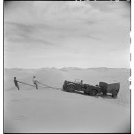 Un tracteur Latil franchit une dune attelé à une remorque, aidé par deux soldats qui tiennent un grillage souple, système d'aide au passage.