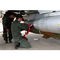 Avant le départ en mission, le pilote en combinaison de vol et un sergent mécanicien de piste effectuent le tour de vérification avant vol de l'avion Mirage 2000D 133-IQ 666 de l'EC (escadron de chasse) 1/3 Navarre : après le contrôle de l'emport de bombe lisse MK-82 250 kg, le mécanicien enlève la flamme.