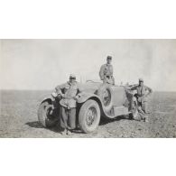 [Portrait de trois militaires autour d'une automobile dans un désert].