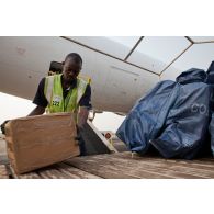 Les colis sont déchargés de l'avion-cargo Boeing 777F d'Air-France KLM par le personnel de l'aéroport de Bangui M'Poko, utilisant un engin convoyeur élévateur Tug.