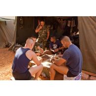 Vie quotidienne sur le camp du 3e RIMa. Un groupe de militaires joue aux dominos devant une tente.