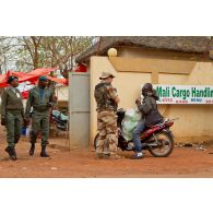Militaire assurant la sécurité des abords du bâtiment du PC (poste de commandement) de la 3e BM (brigade mécanisée), à côté de l'aéroport international de Bamako (Mali). Contrôle d'identité d'un passant en moto.