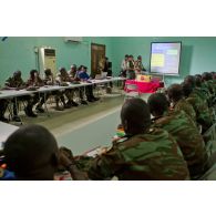 Dans une salle de formation, des stagiaires béninois et sénégalais écoutent le cours sur le droit des conflits armés, dispensé, à l'aide d'un rétroprojecteur, par un commandant ivoirien instructeur, en présence de journalistes de radio dont l'un de France Inter.