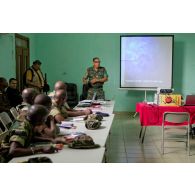 Dans une salle de formation, des stagiaires béninois et sénégalais écoutent le cours sur le droit des conflits armés dispensé par un commandant ivoirien instructeur,à l'aide d'un rétroprojecteur, en présence d'un journaliste de radio avec son microphone.