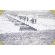 [Un bataillon de chasseurs cyclistes traverse un pont construit par le génie sur une rivière.]