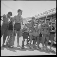 En ville, des enfants attendent en file indienne avant de monter dans leur bus avant leur départ pour le Camp des chasseurs du 8e RIM. [légende d'origine]