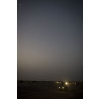 Rame de véhicules en stationnement dans le désert lors de l'arrêt d'un convoi pour la nuit.