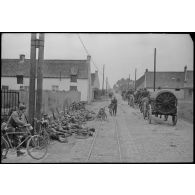 En Belgique, rue de Villiers à Hensies (entre Mons et Valenciennes), des cyclistes allemands prennent du repos, un convoi hippomobile progresse.