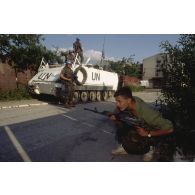 Milicien bosniaque de Sarajevo accroupi armé d'un fusil Kalachnikov AK-74, à proximité d'un blindé M-113 canadien.