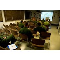 Briefing de préparation de mission pour l'équipage et les opérateurs navigants d'un avion E3F du 36e EDCA (escadron de détection et de contrôle aéroporté) présenté par un capitaine féminin sur la base d'Avord à l'aide d'une carte de Libye.