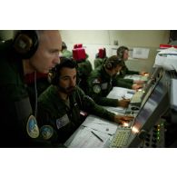 Groupe d'adjudants contrôleurs défense et armes à leurs postes devant les écrans radar aux côtés d'un capitaine, lors d'une mission de contrôle aérien sur la Libye à bord d'un avion de détection Awacs.