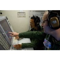 Portrait d'un sergent opérateur d'ESM (electronic support measure ou système d'écoute d'émissions) devant son écran radar aux côtés d'un adjudant-chef, lors d'une mission de contrôle aérien sur la Libye à bord d'un avion de détection Awacs.