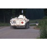Vue de l'arrière d'un véhicule de transport sanitaire russe de type BTR-70 aux couleurs de l'ONU progressant sur une route.