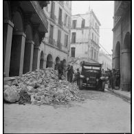 Suite au bombardement allemand de la nuit du 18 au 19 avril 1943, des volontaires de la défense passive déblaient des gravats dans une rue donnant sur la place du Gouvernement à Alger.