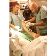 Nettoyage du pansement par les médecins français et allemand sur un patient afghan à la jambe brochée.