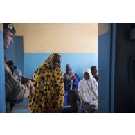 Des civils entrent dans un salle de consultation sous la vigilance d'un légionnaire du 2e REP, lors d'une AMP au dispensaire du village de Tiloa.