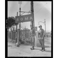 Le lieutenant general Mark Wayne Clark, commandant la 5e armée américaine, pose symboliquement devant un panneau indicateur aux portes de Rome libérée ; à ses côtés, l'un de ses grands subordonnés, le major general Geoffrey Keyes, commandant le 2e corps d'armée.