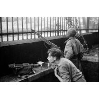 Dans Saulxures-sur-Moselotte occupé par le 3e RTA, un tirailleur fait sa toilette pendant que son camarade veille avec son fusil-mitrailleur BAR.