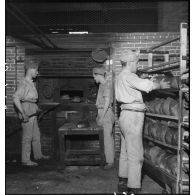 Des soldats boulangers enfournent des pains dans un four dans une boulangerie de l'intendance militaire.