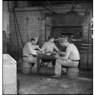Des soldats boulangers se restaurent en surveillant la cuisson du pain dans une boulangerie de l'intendance militaire.