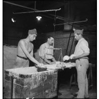 Des soldats boulangers pétrissent la pâte à pain dans une boulangerie militaire.