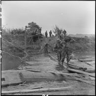 Des éléments du 35e régiment d'artillerie légère parachutiste (RALP) et des partisans franchissent la rivière Nam Youn chargés d’un canon de 75 mm sans recul largué par parachute.