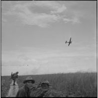 Suite à des tirs de mitrailleuse Vietminh, des fantassins de la 5e compagnie du 2e bataillon du 43e régiment d’infanterie colonial (43e RIC) se tiennent en position derrière le talus d'une rizière, au cours de l'opération Tourbillon 2. Un avion de reconnaissance les survole.