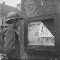 [Un fantassin de la 42e DI (division d'infanterie) se trouve dans une rue de Lauterbach (Sarre) devant un panneau du journal de la Waffen-SS 