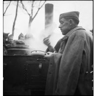 Debout gamelle en main, un soldat de la 2e armée mange près d'une cuisine roulante.