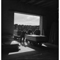 Des soldats de la 5e armée poussent des wagonnets chargés de planches à l'intérieur de l'atelier.