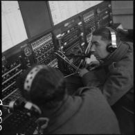 Deux soldats utilisent des appareils de transmissionss dans un central téléphonique.