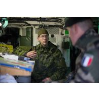 Un soldat du 501e régiment de chars de combat (501e RCC) discute avec son homologue canadien à bord d'un véhicule de combat LAV 6 à Kadaga, en Lettonie.
