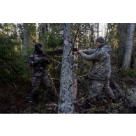 Un instructeur estonien aide un soldat à scier un tronc d'arbre en forêt de Järvama, en Estonie.