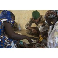Un médecin du 2e régiment étranger de parachutistes (REP) soigne un enfant dans les bras de sa mère à l'école de santé de Ménaka, au Mali.