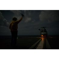 Un chien jaune guide le décollage d'un hélicoptère Panther AS-565 de la flottille 36F depuis la frégate de surveillance Ventôse pour une mission nocturne en mer des Caraïbes.