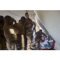 Des instructeurs du Service de santé des armées (SSA) encadrent l'installation de l'équipement médical à l'intérieur d'un module sanitaire par des stagiaires burkinabè à Dori, au Burkina Faso.