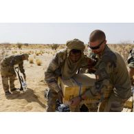 Un sapeur du 6e régiment du génie (6e RG) aidé d'un soldat malien exhume une caisse de munitions enfouie dans le sable en vallée d'Inaïs, au Mali.
