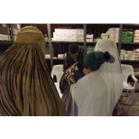 Consultations pour la population civile à l'hôpital jordanien de l'aéroport de Mazar e Charif. Femmes afghanes voilées venues consulter, l'une portant un enfant, au comptoir de la pharmacie.